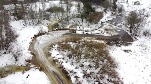 Aerial drone view of a river meandering around a corner in the winter forest. Recorded in Vahiküla Falls, Estonia.