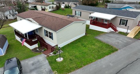 Small mobile home in trailer park, bungalow, manufactured home close to other houses, patriotic American flag, beautiful landscaping, United States of America USA aerial establishing shot in winter.