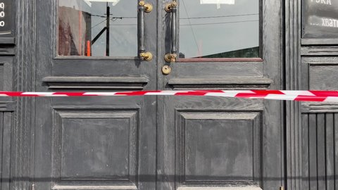 4K video with closed wooden doors of a bar or restaurant. Red and white border tape. Translation from Russian: Enough