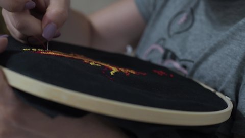 a young woman embroiders a picture with threads according to the instructions. the black canvas is covered with multicolored threads