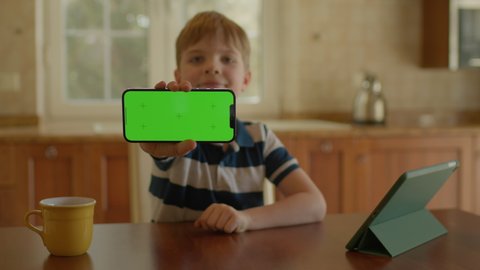 School boy using mobile phone and showing green screen at camera. Kid holding horizontal chroma key mobile phone screen.