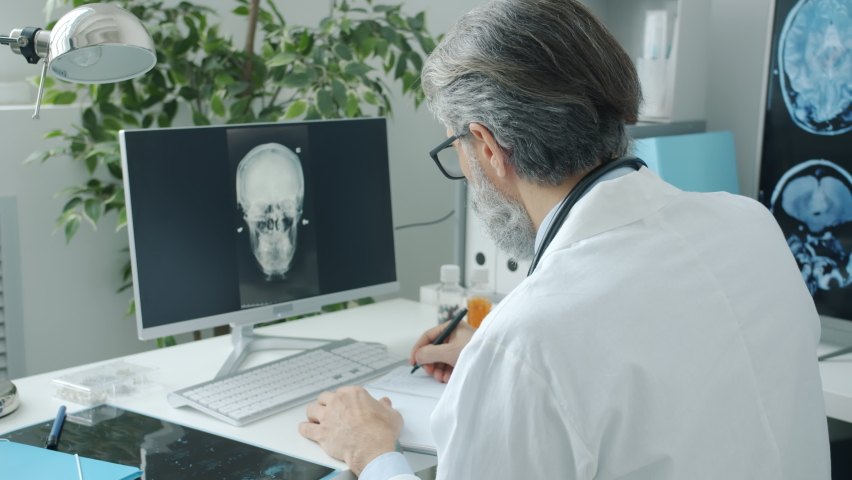Doctor neurologist looking at human brain MRI images on computer screen and writing in clinic. Hospital routine and modern technology concept. Royalty-Free Stock Footage #1088553587