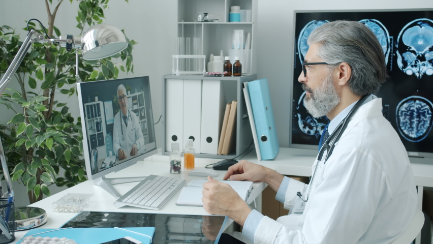 Doctors colleagues making online video call talking waving hand using PC in hospital. Modern technology and virtual meeting concept. Royalty-Free Stock Footage #1088553613