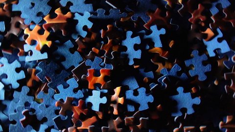 Background of Colored Puzzle Pieces that Rotating Counterclockwise - Top View. Texture of Incomplete Red and Blue Jigsaw Puzzle with Low Key Light - Left Rotation