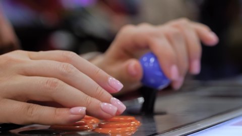 Close up view: woman hands playing retro arcade machine game and pushing orange buttons - selective focus. Gaming, 80s, hobby, vintage, technology, retro video game and leisure time concept
