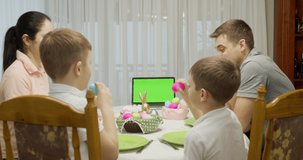 green screen notebook. Parents with two teenage boys talking video call using a laptop, enjoying spending time together on the weekend, at home, at the holiday table prepared for Easter