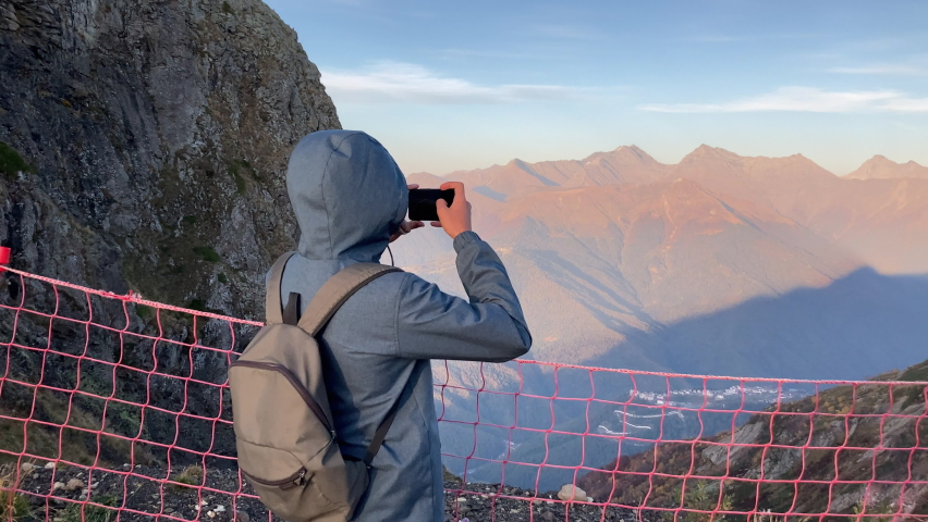 Young adult man tourist take photo on phone at background mountain back view. Guy shooting mobile on vacation. Trip to mountains. Male tourism leisure people. Person taking photo on phone traveling. Royalty-Free Stock Footage #1088557015