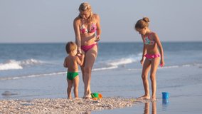 A kind, caring, beautiful mother plays with her children: the eldest skinny daughter and the youngest son, a toddler, building beads and sand castles decorating them with shells and pebbles