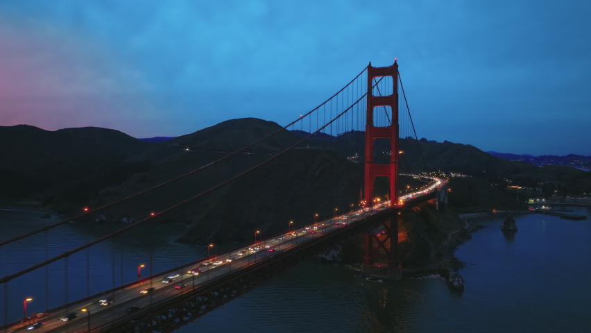4K aerial night city illumination. Golden Gate Bay Bridge at night time. Vehicles in busy traffic 101 highway at scenic suspension Red Bridge with cinematic pink sunset. San Francisco California USA