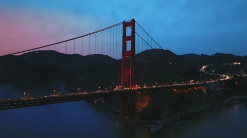 4K aerial night city illumination. Golden Gate Bay Bridge at night time. Vehicles in busy traffic 101 highway at scenic suspension Red Bridge with cinematic pink sunset. San Francisco California USA