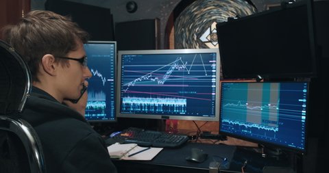 Man freelance trader on stock exchange, trades while sitting at a computer, he discusses growth and fall charts on the phone. Concept of game on stock exchange for trading stocks, futures and bonds