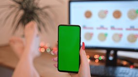 A woman orders pizza. Woman in her office is holding a smartphone with a green screen. The girl chooses pizza on the site.
