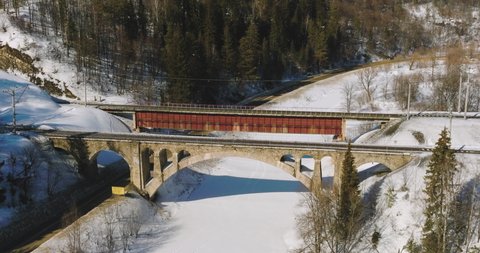 Stone and iron railway bridge by dangerous part of Trans Siberian railways near river in forest mountains. Aerial drone wide view at winter sunny day