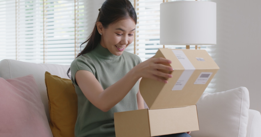 Young happy asia people teen girl smile enjoy unbox post mail sit relax at home comfort sofa couch feel joy amazed awe wow in omni channel fast send parcel via online sale shop store e-commerce order. | Shutterstock HD Video #1088565261