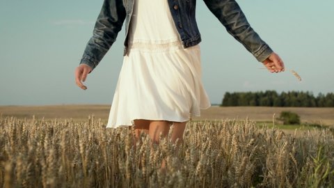 Girl rotating around herself in wheat field. Her white dress beautifully floats in the air. Woman is happy and full of positive energy. She is celebrating something or enjoying warm summer evening.