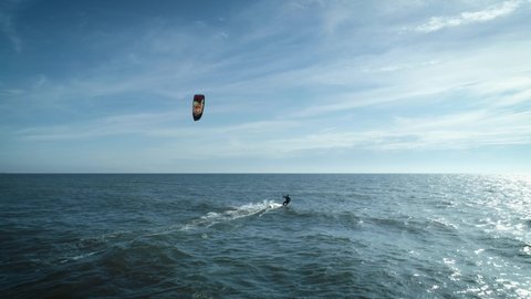 In this aerial drone camera shot you can see fearless extreme sport lover – kiteboarder riding ocean water with his kite flying in the blue sky.