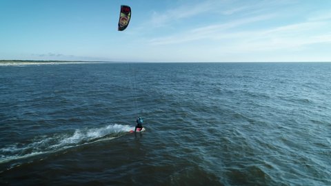In this aerial drone camera shot you can see fearless extreme sport lover – kiteboarder riding ocean water with his kite flying in the blue sky.