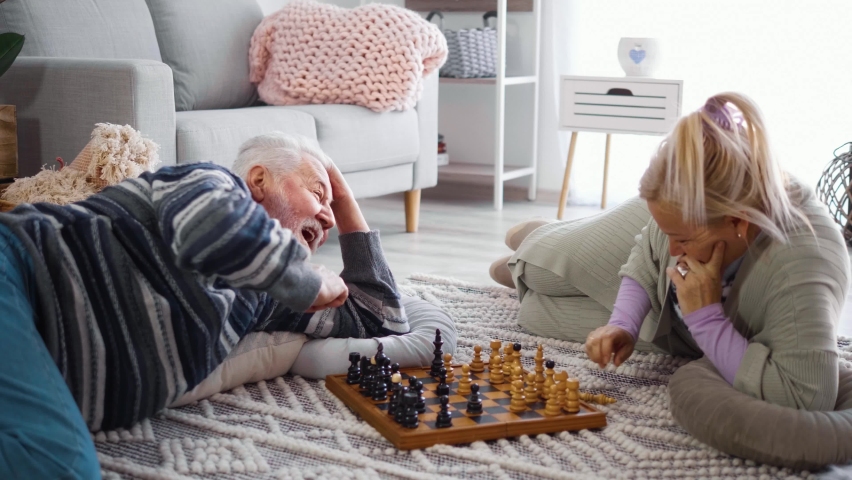 Cheerful old man sincerely laughs while playing chess with an older woman at home lying on the floor. - Powered by Shutterstock - Get 15% off with code: PIKWIZARD15