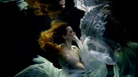 mysterious woman and head of mythical dragon in depth of magical sea or ocean, underwater fantasy