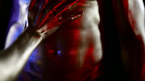 close-up of a female hand on a muscular male body with golden metallic skin. red, blue and white light. the dark key. without faces