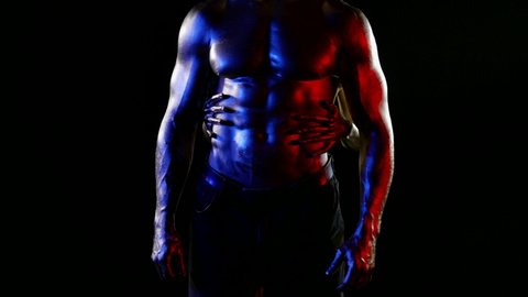 the middle plan of a muscular male torso with golden metallic skin. a woman stands behind a man and strokes stomach with her hands. red, blue and white light. without faces. dark key