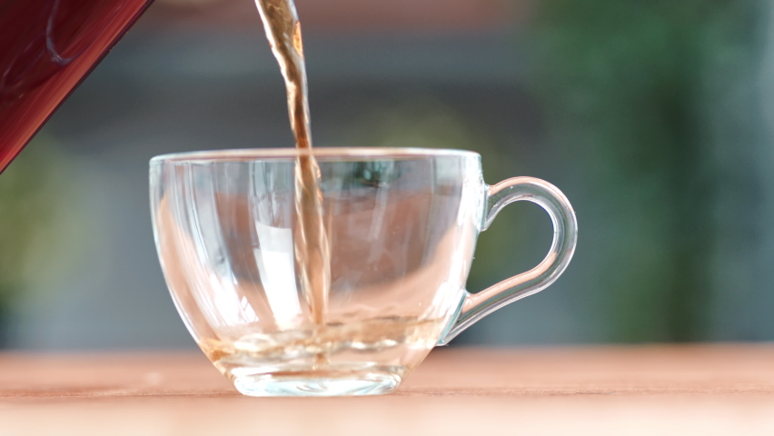 Closeup pouring stream fresh aroma hot black tea into transparent glass cup from teapot serving breakfast wooden table. Adding fragrance refreshment herbal beverage to elegant mug slow motion Royalty-Free Stock Footage #1088568333