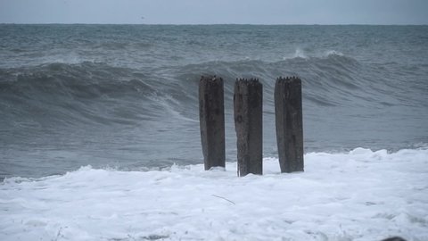 Storm waves crash against old reinforced concrete pillars on the beach, a cloudy spring day. Storm at sea. slow motion. Cloudy weather. Batumi Georgia,