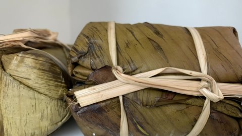 4K Time Lapse Thai traditional sweet banana wrapped with sticky rice by banana leaf defrosting on a white background. Strings made of shredded banana stems from banana tree. In Thai is "Khao Tom Mad"
