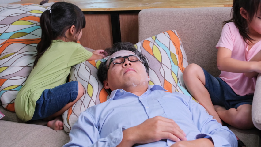 Cute little sisters doing makeup and hair for dad to sleep on the sofa at home. Happy Father