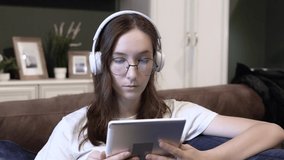 A girl at home wearing headphones and a tablet with glasses. Online lessons
