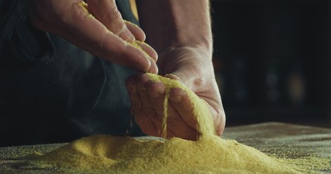 Cinematic close up shot of professional baker chef sprinkles corn flour dust powder on table while kneading dough for preparation of breads, gluten-free baking and fried foods in rustic bakery kitchen