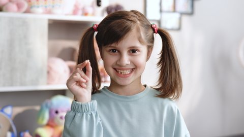 Portrait of cute little child girl is rejoices and showing her lost milk tooth and smiling to camera of toothless mouth while she standing in bedroom. Happy girl holding her fallen tooth in hand