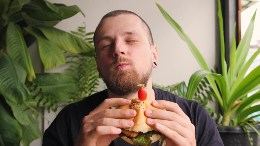 Handsome Bearded Man Eating Vegan Burger in Restaurant Enjoying Delicious Plant Based Meal. Healthy Fast Food High Quality 4K Concept Footage.