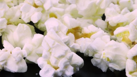 Macro shot of tasty popcorn rotating on black surface, close up view.