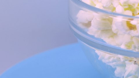 Bowl of popcorn rotating over a blue surface, macro shot in 4k.