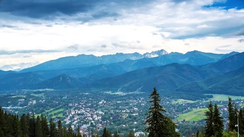 top of Poland Mountains mount gubalowka looking at Tatra Mountains town below with rolling clouds loving over the mountain peaks zakopane green trees over looking the valley