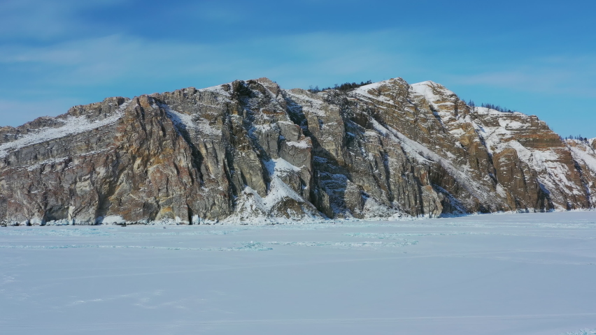Aerial around view of Rocky shore of Olkhon Island on frozen Lake Baikal. Siberia, Russia, 4k