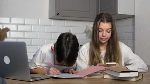 The boy does his homework and shows the results to his older sister. The girl looks at the phone and ignores her younger brother. Study