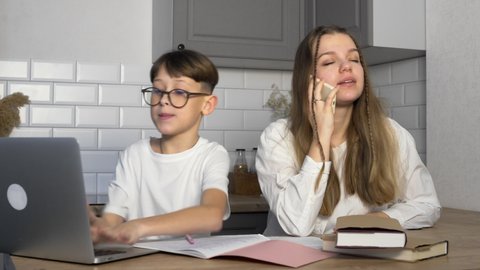 The boy does his homework and shows the results to his older sister. The girl is talking on the phone and ignores her younger brother. The boy demands attention. Study