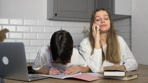 The boy does his homework and shows the results to his older sister. The girl is on the phone and ignores her younger brother. Study