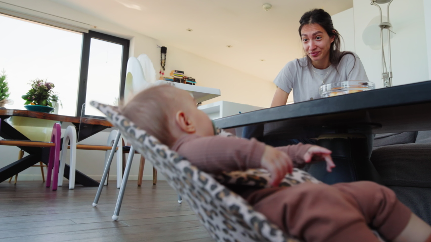 Mom gesturing at her baby that is swinging in a crib.