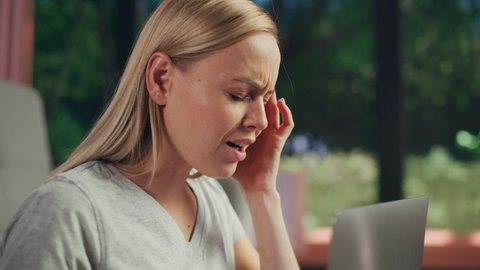 Close Up of a Young Adult Female Working on Laptop Computer and Experiencing Discomfort and Migraine. Tired Woman Having Sudden Serious Headache while Working at Home.