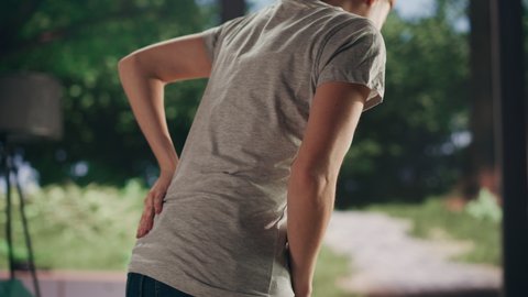 Close Up of a Young Adult Female Standing Up from a Couch at Home and Experiencing Back Pain in a Result of Spine Trauma. Massaging and Stretching the Back to Ease the Discomfort and Injury.