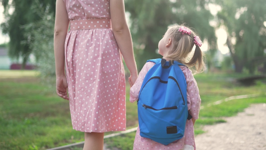 Happy family in park. Mom and daughter go to school hand in hand. Schoolgirl with backpack goes to school in park.Family back to school. Mom and daughter with backpack walk holding hand.Back to school Royalty-Free Stock Footage #1088579017