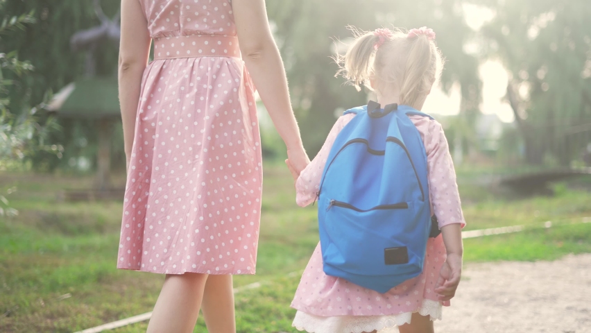 Happy family in park. Mom and daughter go to school hand in hand. Schoolgirl with backpack goes to school in park.Family back to school. Mom and daughter with backpack walk holding hand.Back to school