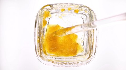 Marijuana concentrate wax in a small glass container, being used with a glass dabber.  Close up macro video of THC concentrate, ready for use in a dab or concentrate smoking device.
