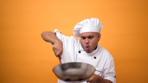 Portrait of happy man chef cooking with pan and turner with a serious expression on isolated yellow background.