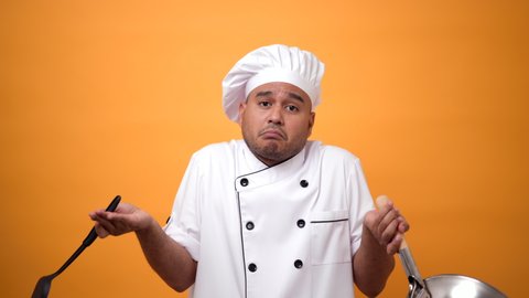 Portrait of unhappy man chef with pan and turner with a serious expression on isolated yellow background.