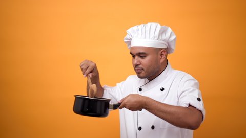 Portrait of happy man chef cooking with pot and turner on isolated yellow background.