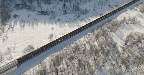 Freight train with empty railway carriages on winding two-sided in wild mountains landscape through a difficult part of Trans Siberian railways - Aerial drone view at winter sunny frozen day